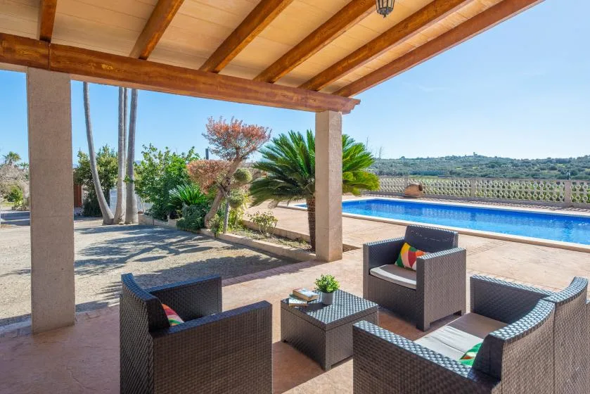 A covered outdoor patio with seating overlooks a swimming pool and landscaped grounds.