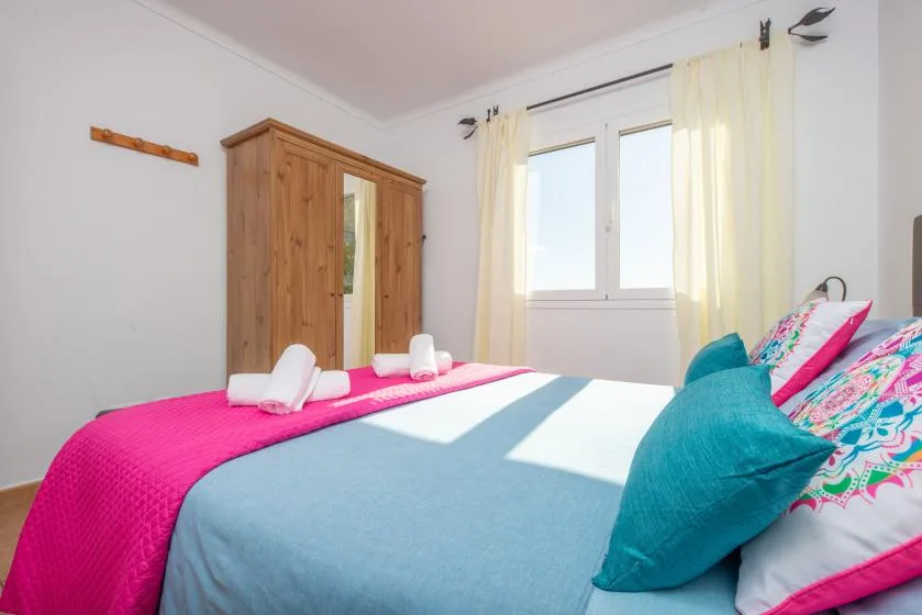 A bedroom with a bed dressed in bright pink and blue bedding.