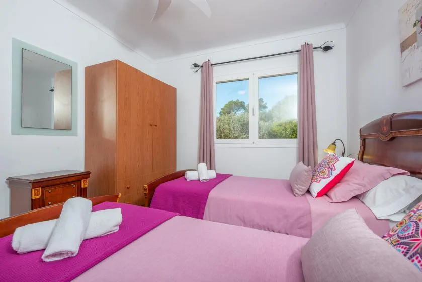 A bedroom with two beds and a window overlooking greenery.