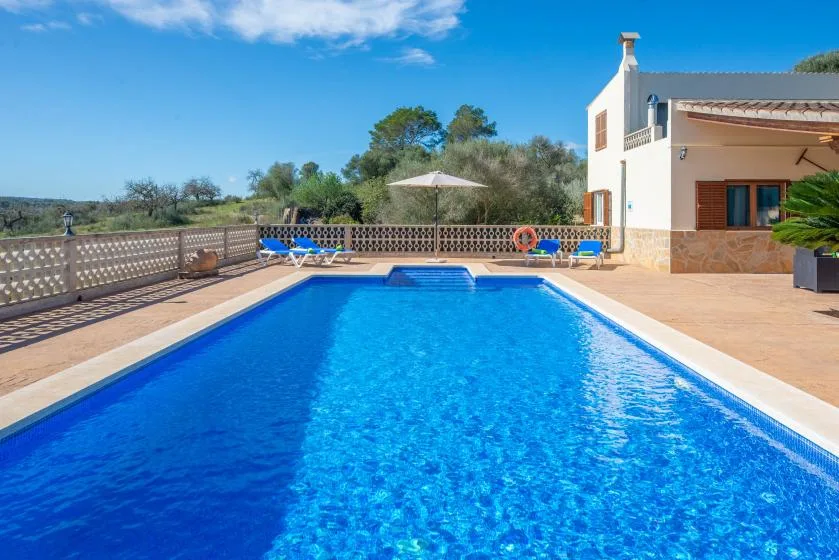 An outdoor swimming pool beside a house, with lounge seating and an umbrella.