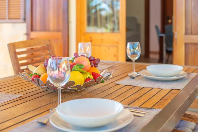 A dining table is set with plates, glasses, and a bowl of fresh fruit.