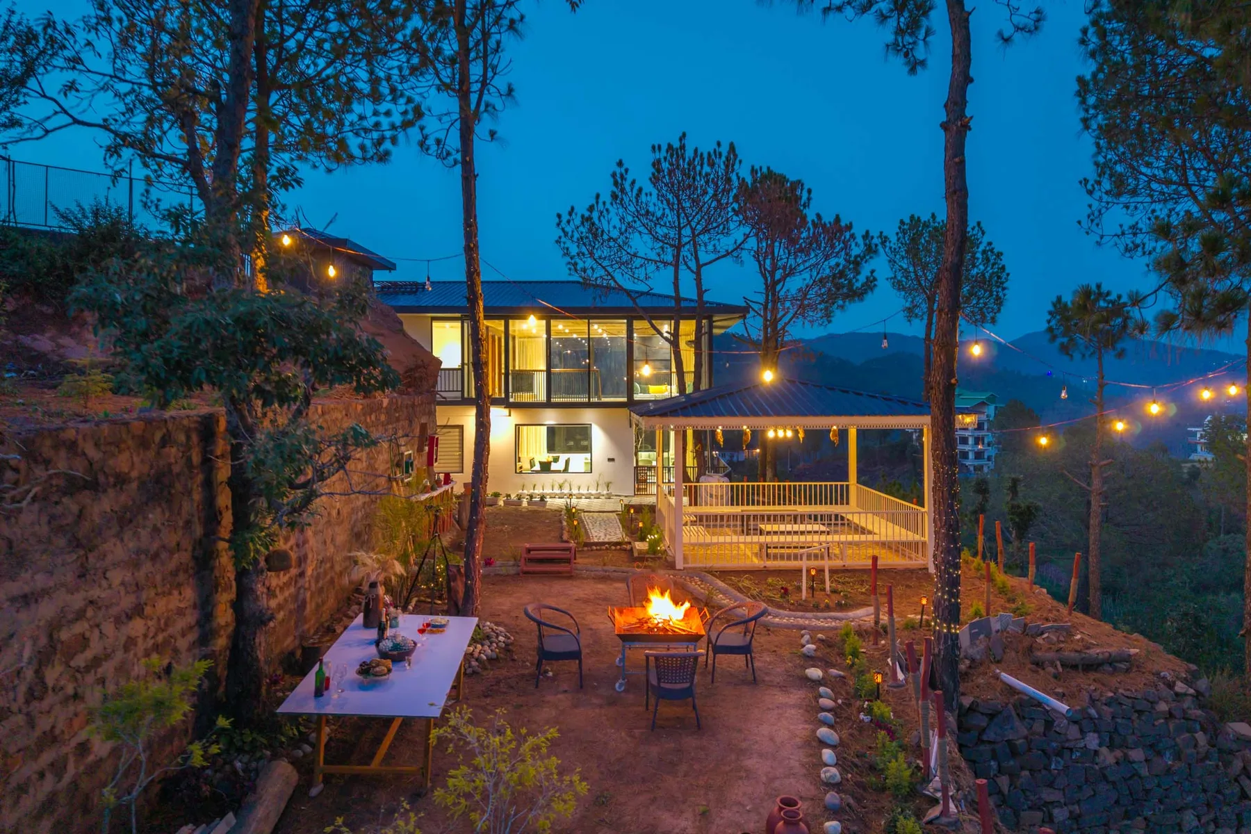 An outdoor patio beside a warmly lit building, with seating around a fire pit.