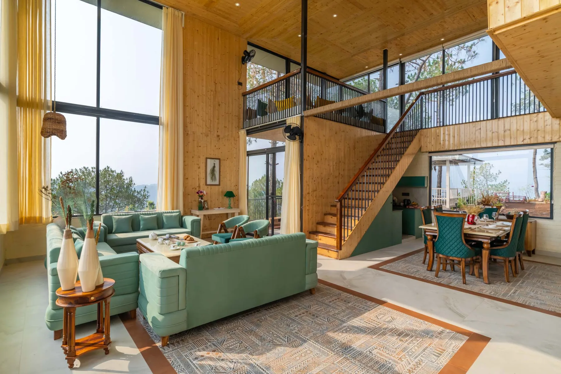 A high-ceiling living and dining area with teal seating beneath an open staircase.
