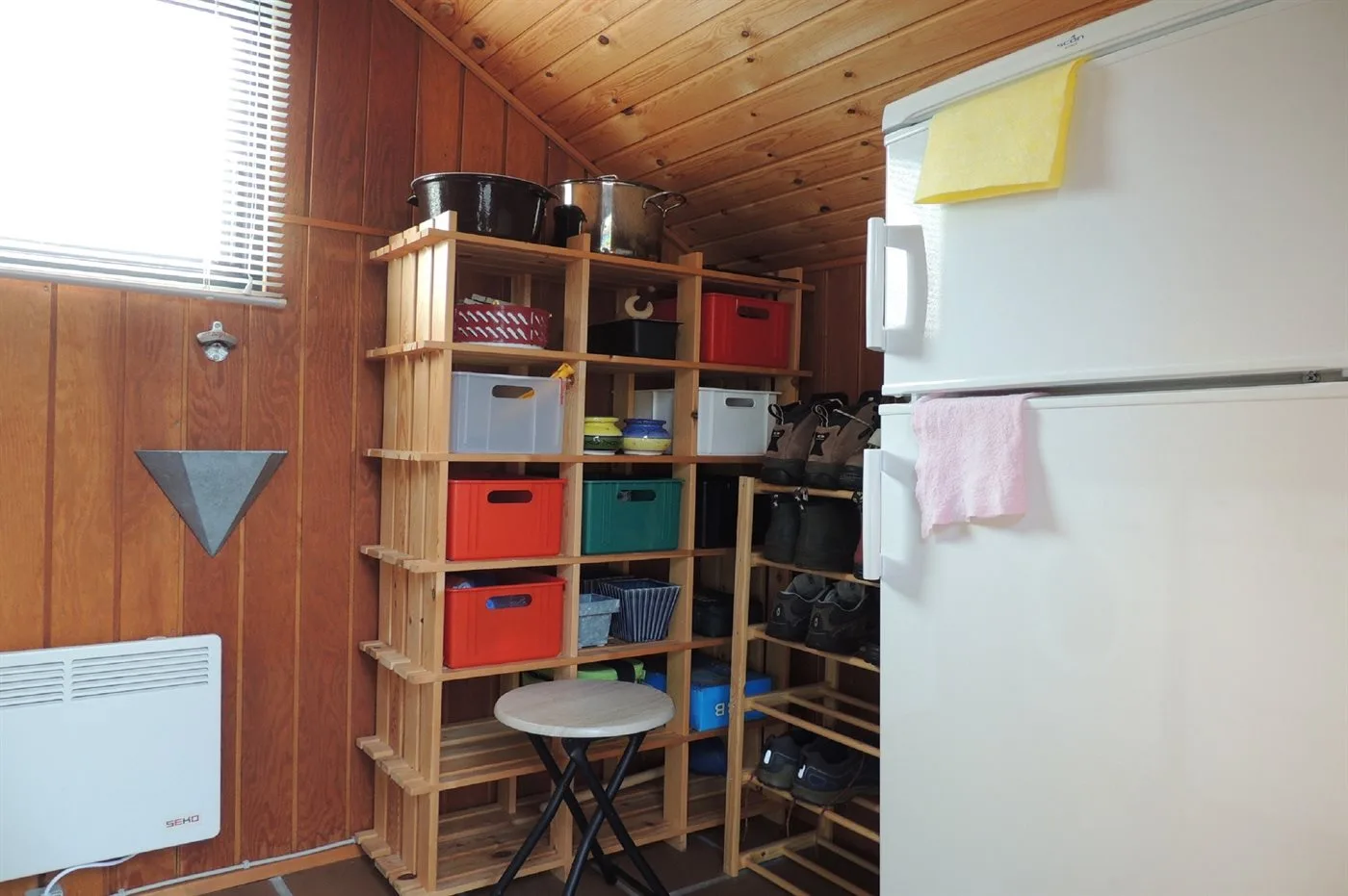 Un cuarto de almacenamiento revestido de madera con estantes abiertos y un refrigerador.