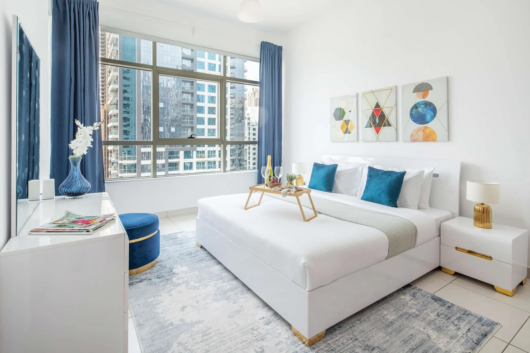 A bright bedroom with a white bed, blue accents, and large windows.