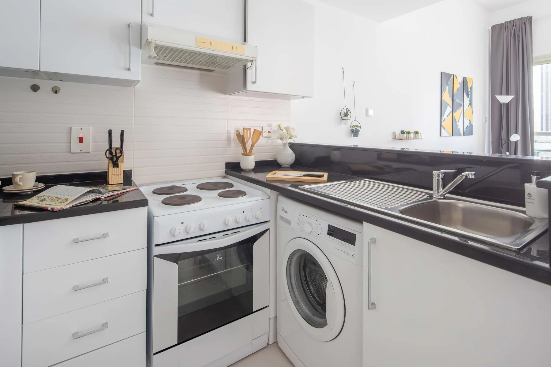 A bright kitchen with a stove, washing machine, and sink along the counter.