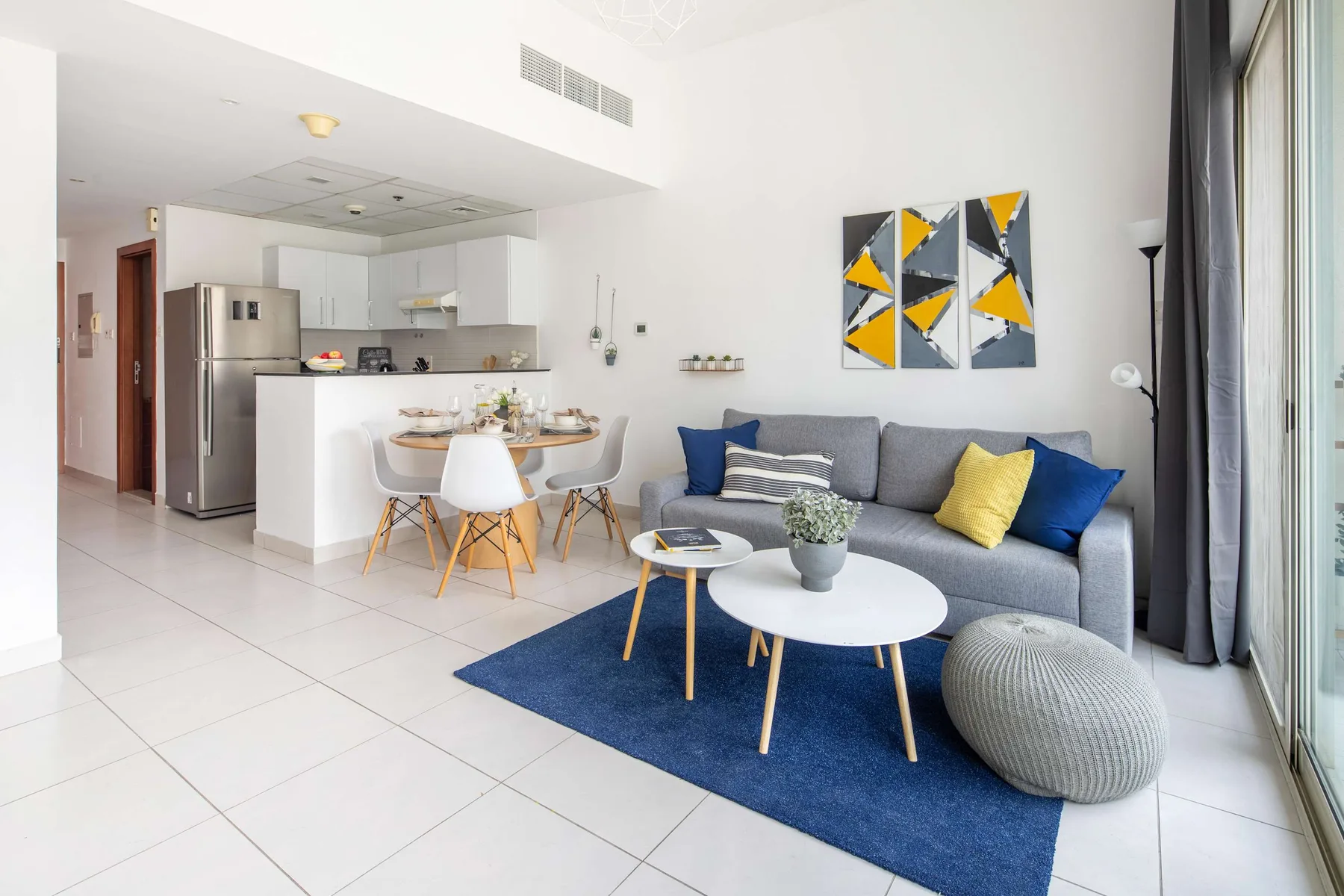 A bright living room with a gray seating area, blue rug, and open kitchen.