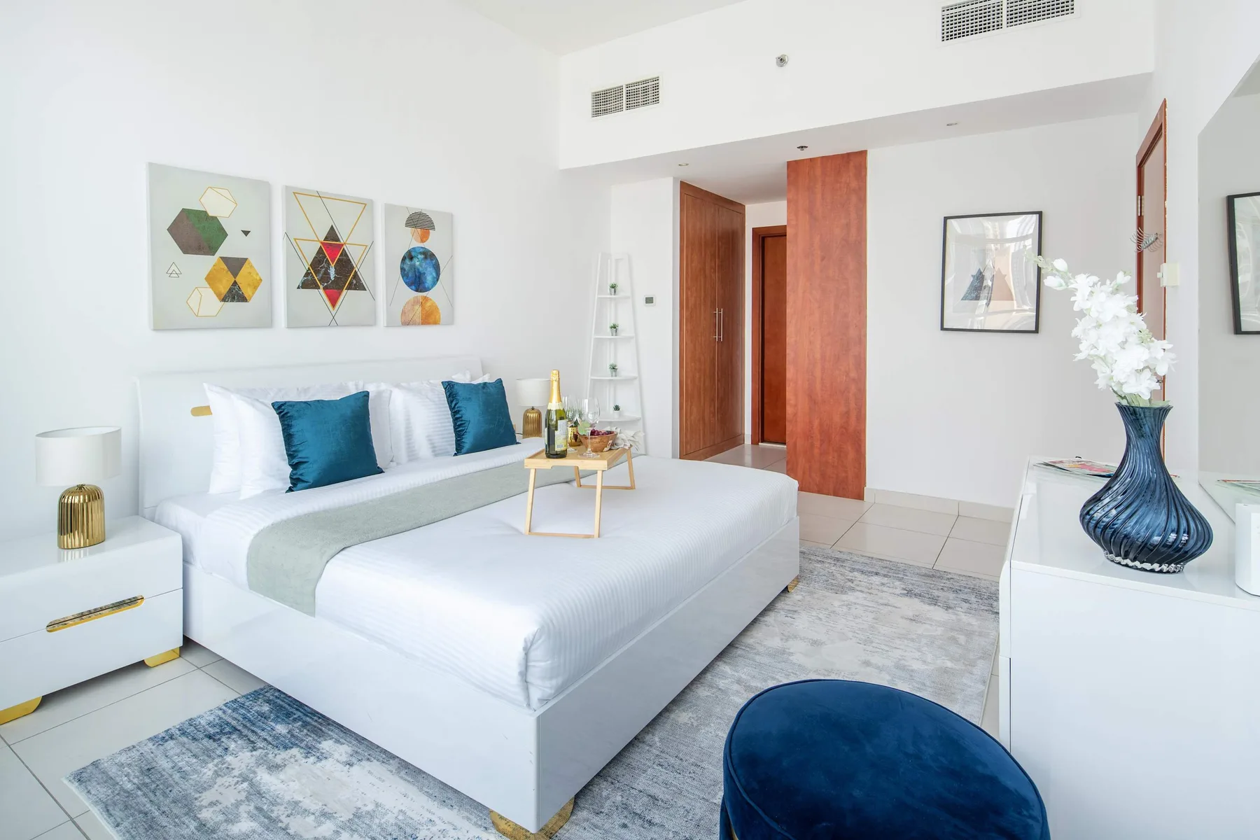 A bright bedroom with a neatly made bed and colorful geometric wall art.
