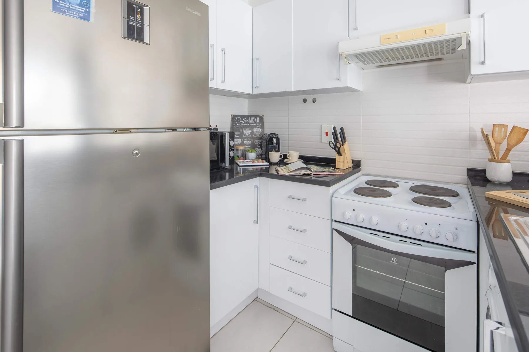 A bright kitchen with white cabinets, a stainless steel refrigerator, and an electric range.
