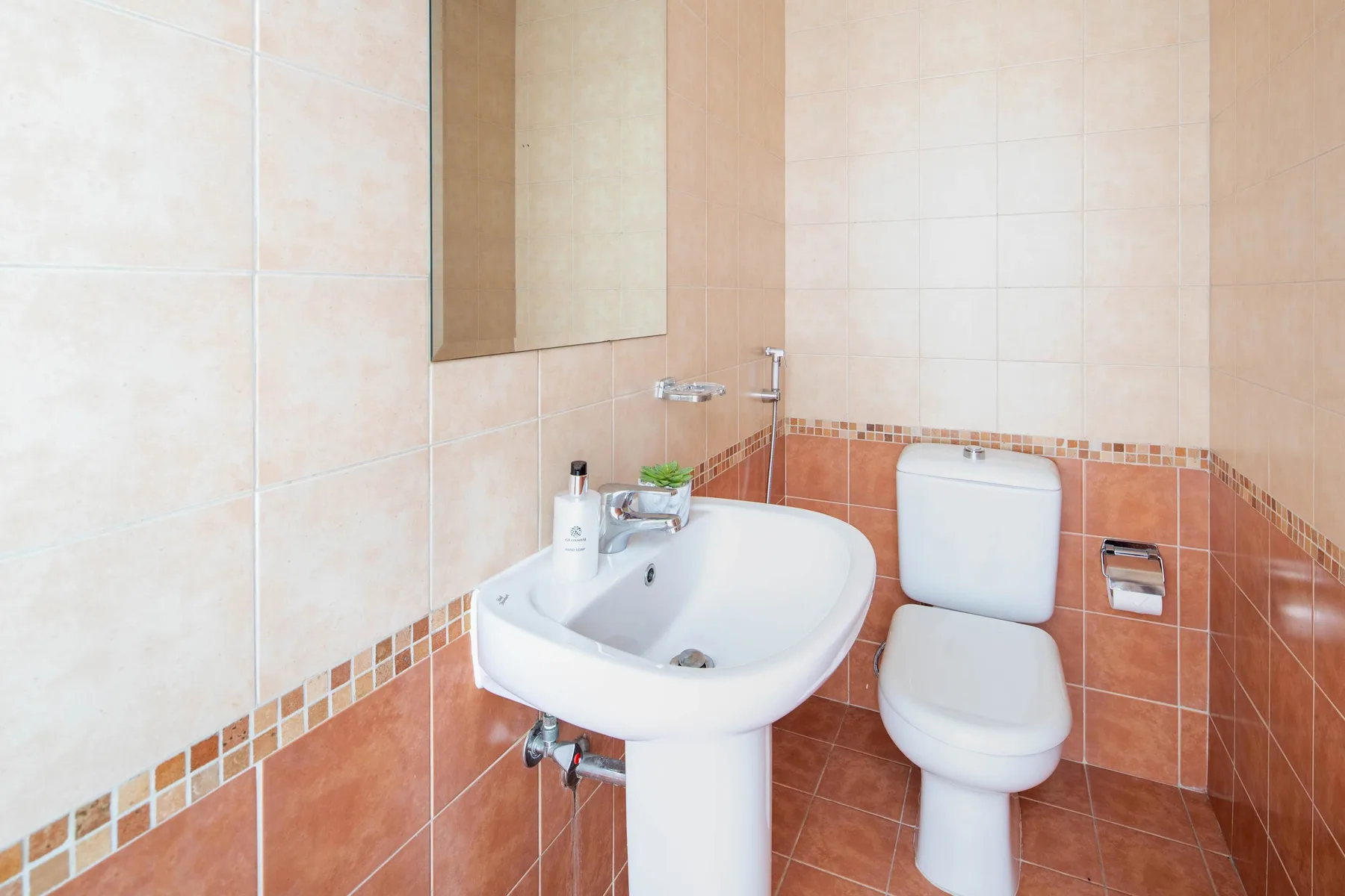 A tiled bathroom with a wall-mounted sink and toilet.