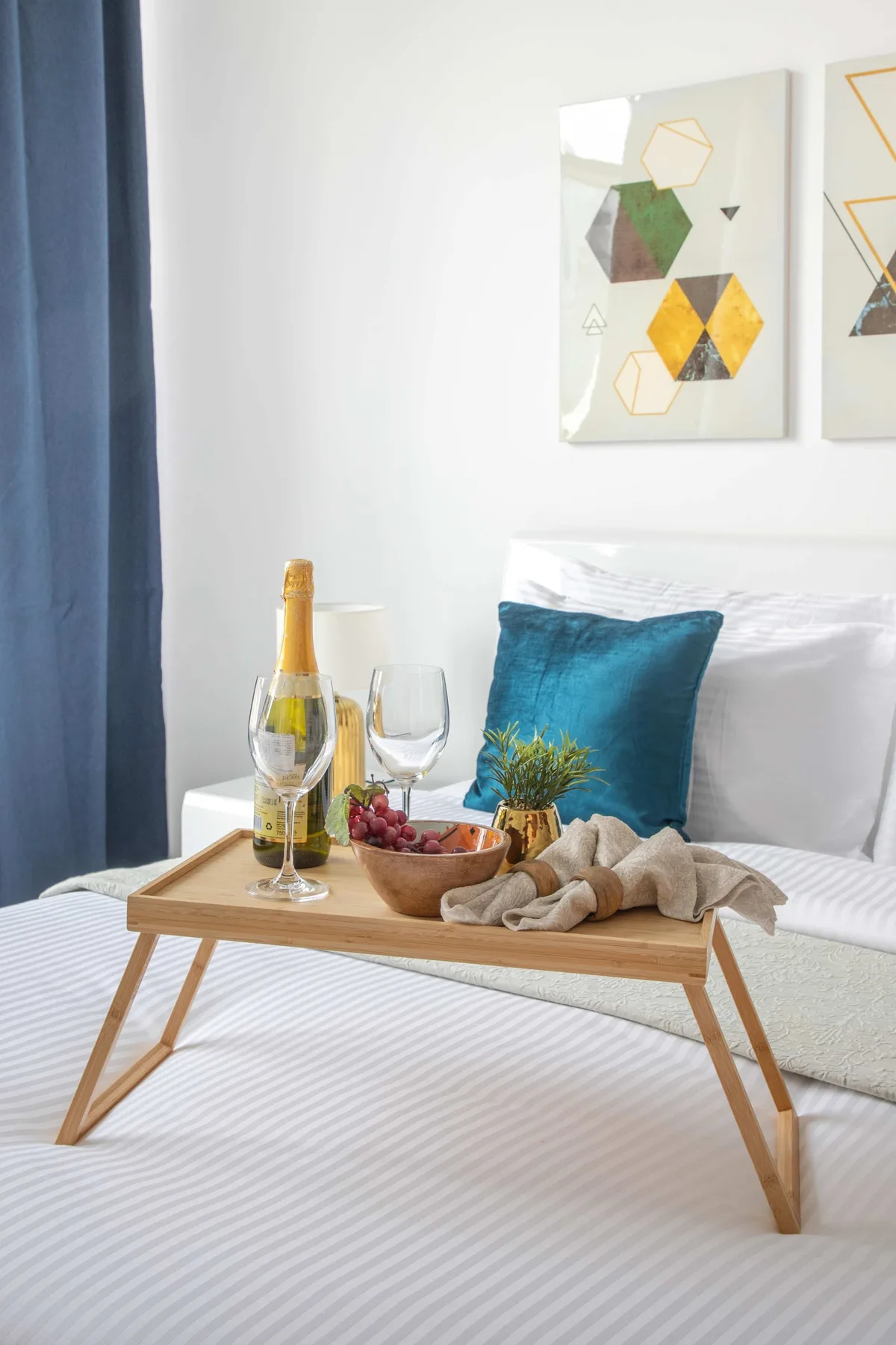 A bedroom with a bed, a teal cushion, and a tray of refreshments.