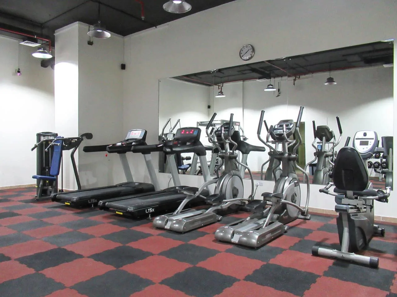 A gym with treadmills and other exercise equipment in front of a wall mirror.