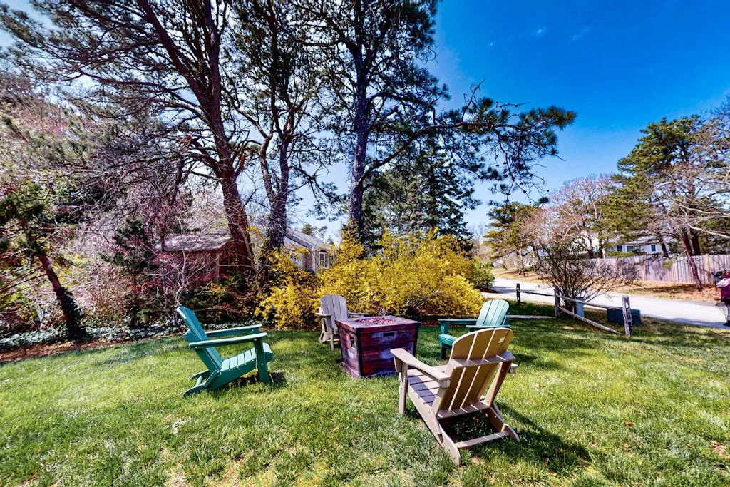A grassy outdoor seating area with colorful chairs beneath trees.