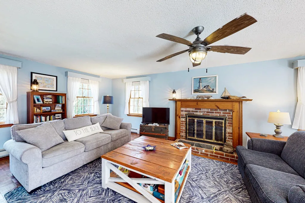A living room with seating arranged around a wooden coffee table and fireplace.