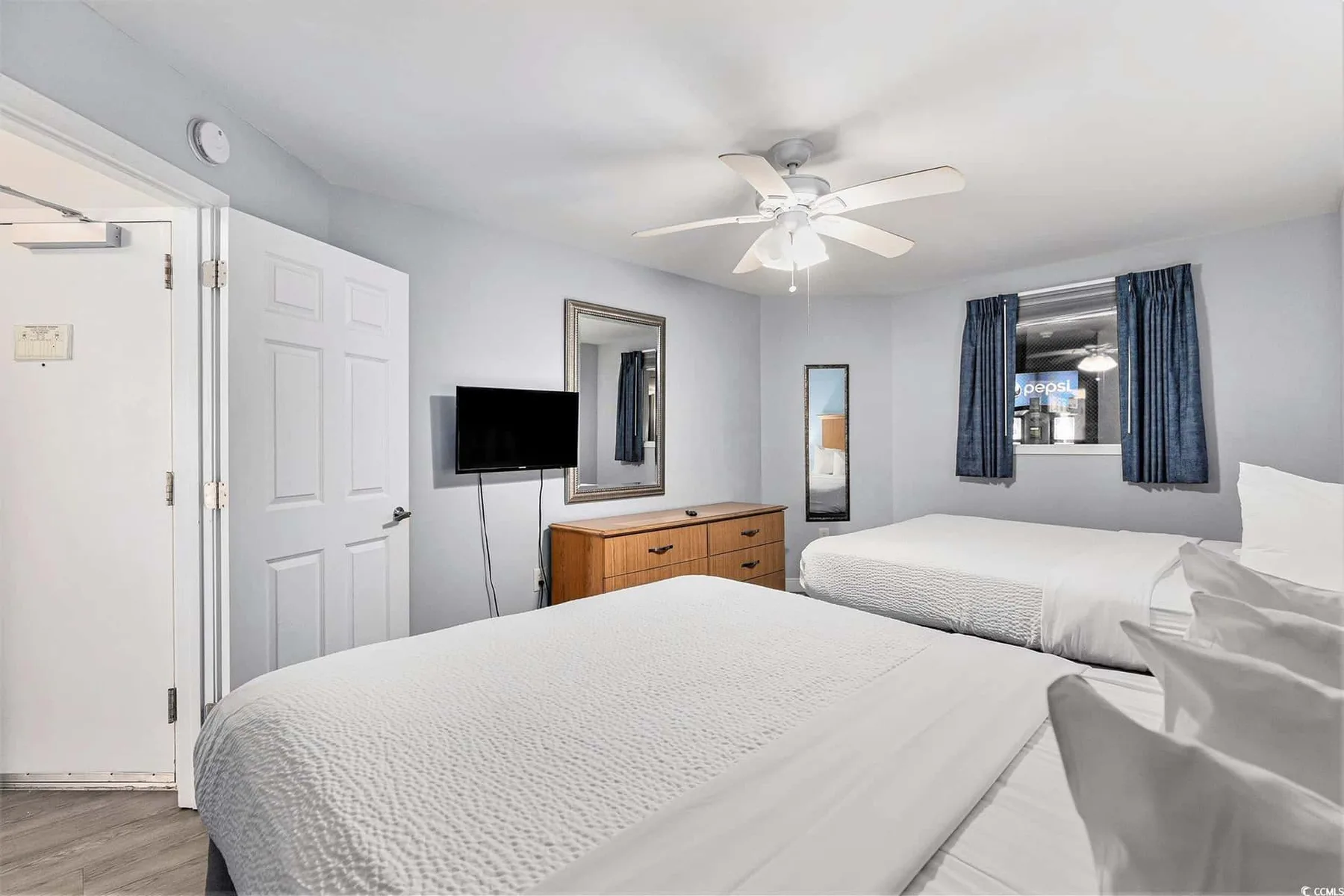 Bedroom with two beds, a television, and a window with curtains.
