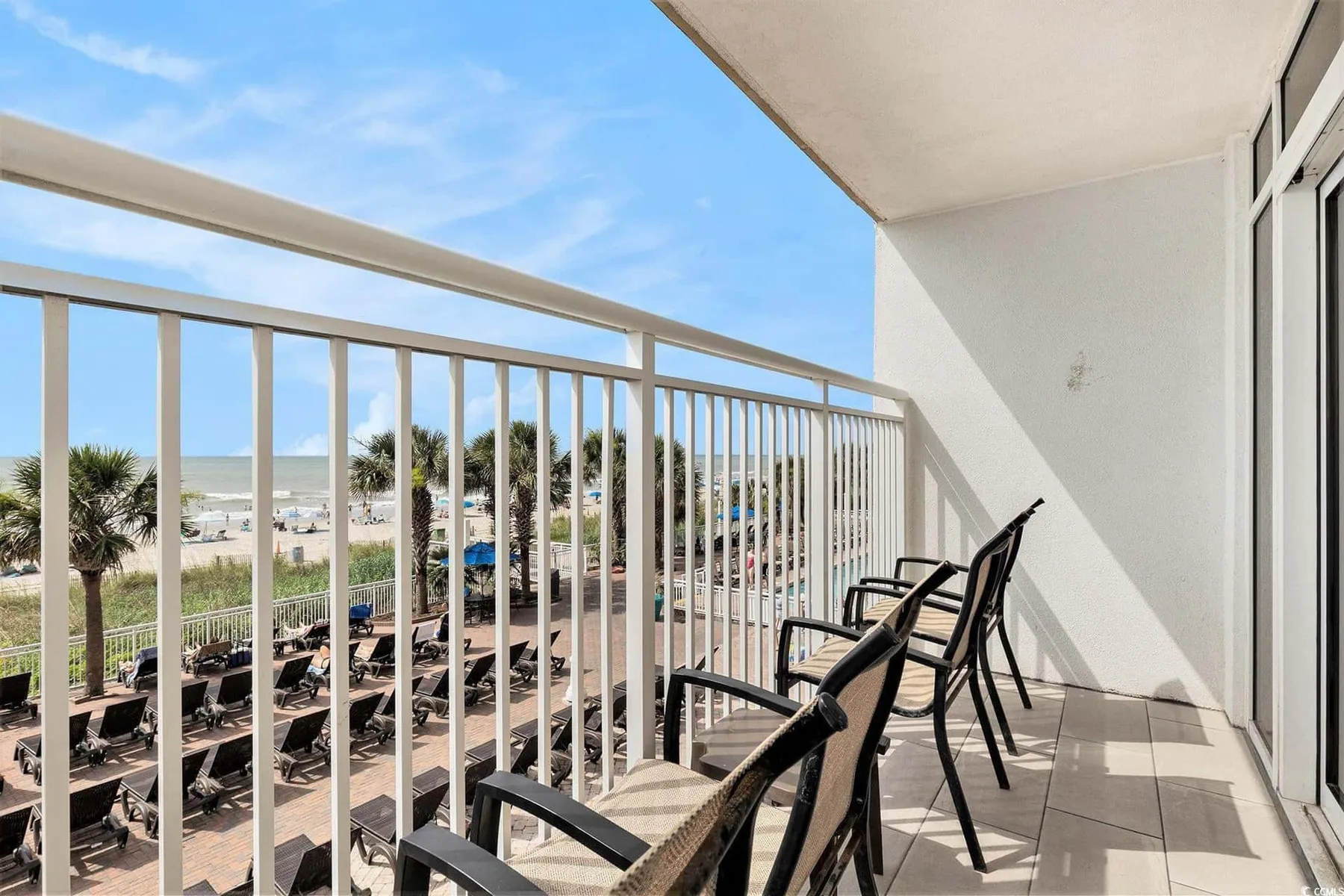 A balcony with outdoor seating overlooks the beach and ocean.