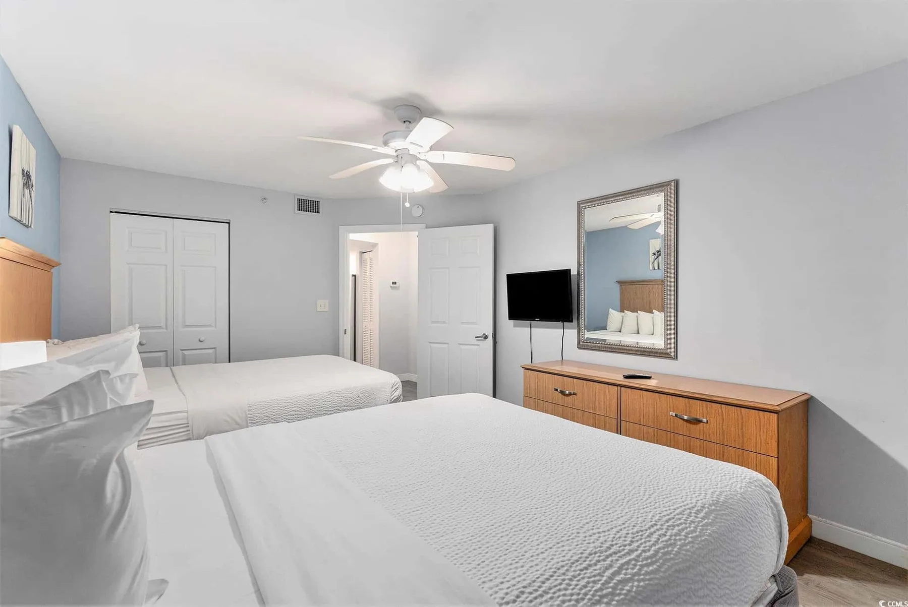 A bedroom with two beds, a ceiling fan, and a dresser.