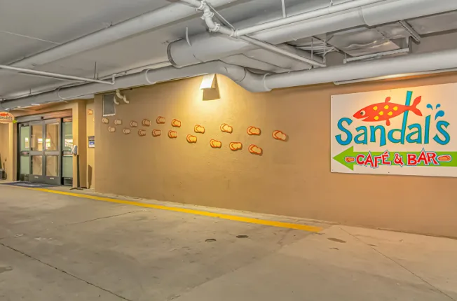 An indoor parking area has a concrete floor, exposed ceiling pipes, and a café sign.