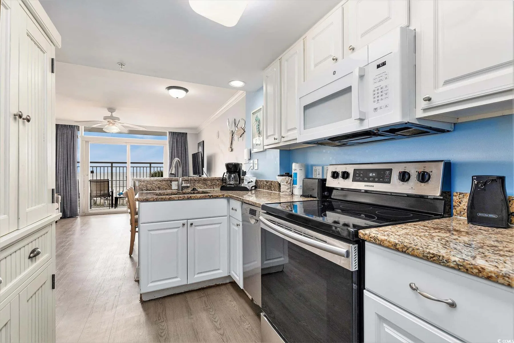 A bright kitchen with white cabinets and a countertop, opening onto a balcony.