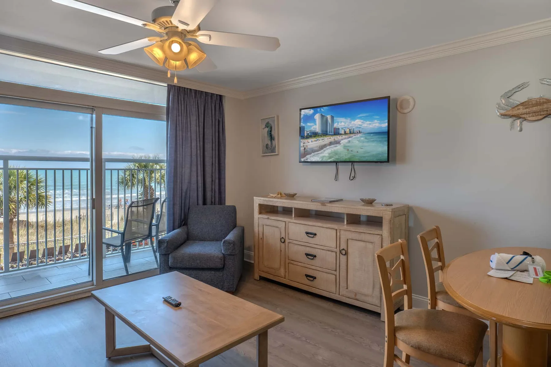 A living and dining area with seating, a television, and a balcony overlooking the water.