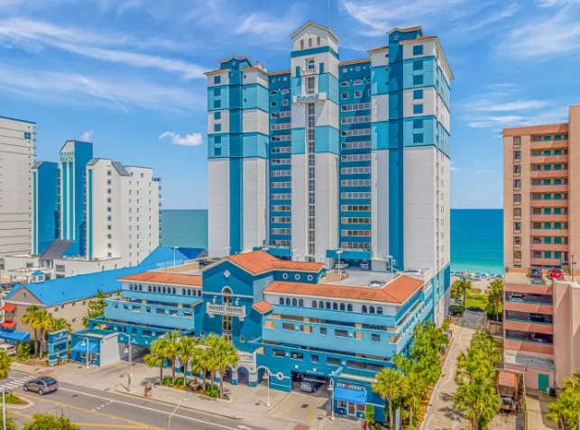 A blue high-rise building stands beside the ocean under a clear sky.