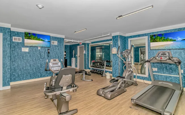 A fitness room with exercise machines and a wall-mounted television.