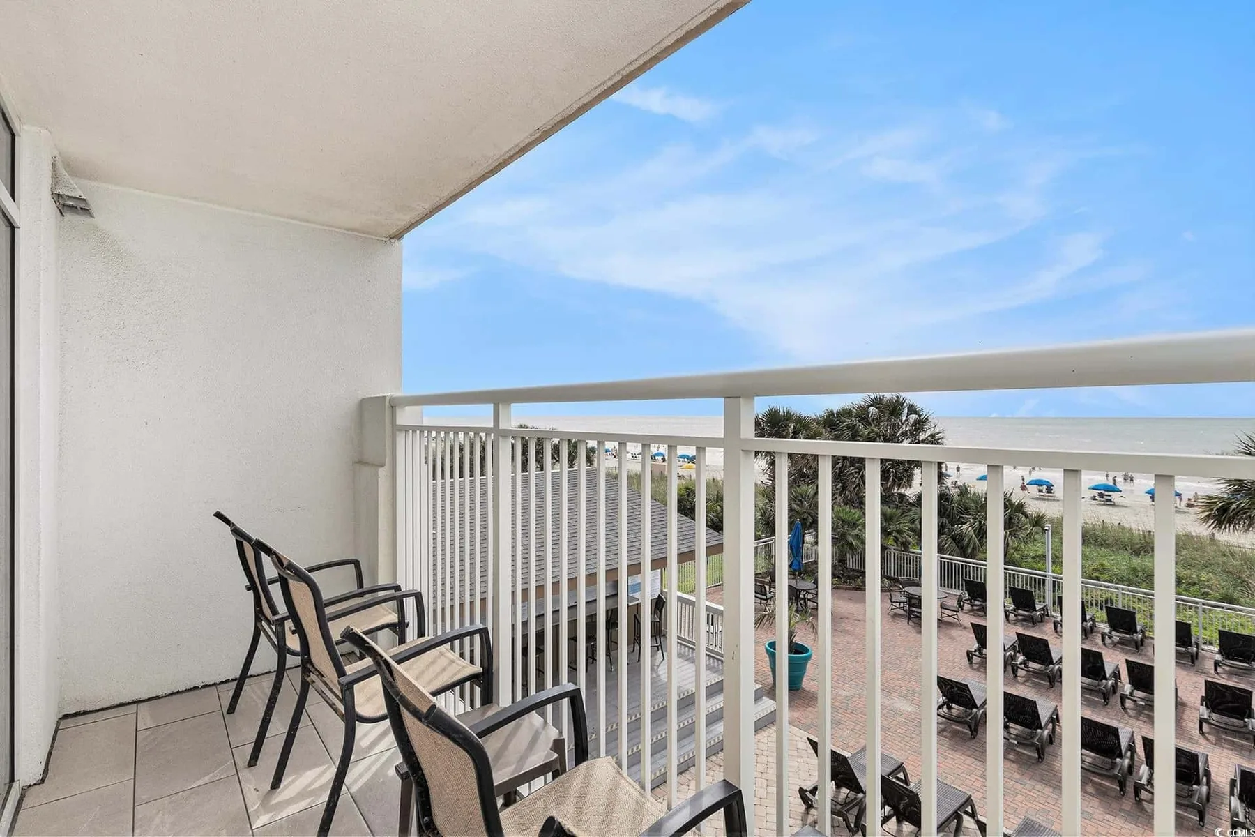 A balcony with seating overlooks a pool deck and the ocean.
