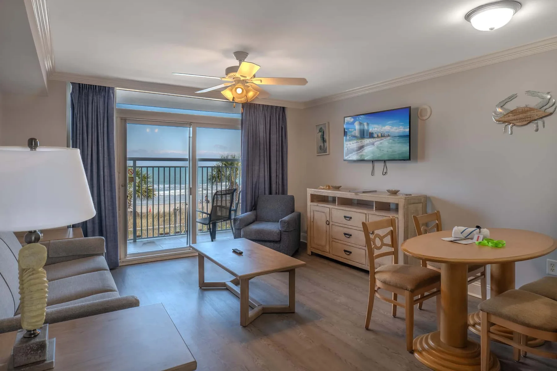 A living and dining area with seating, a television, and a glass door opening onto a balcony.