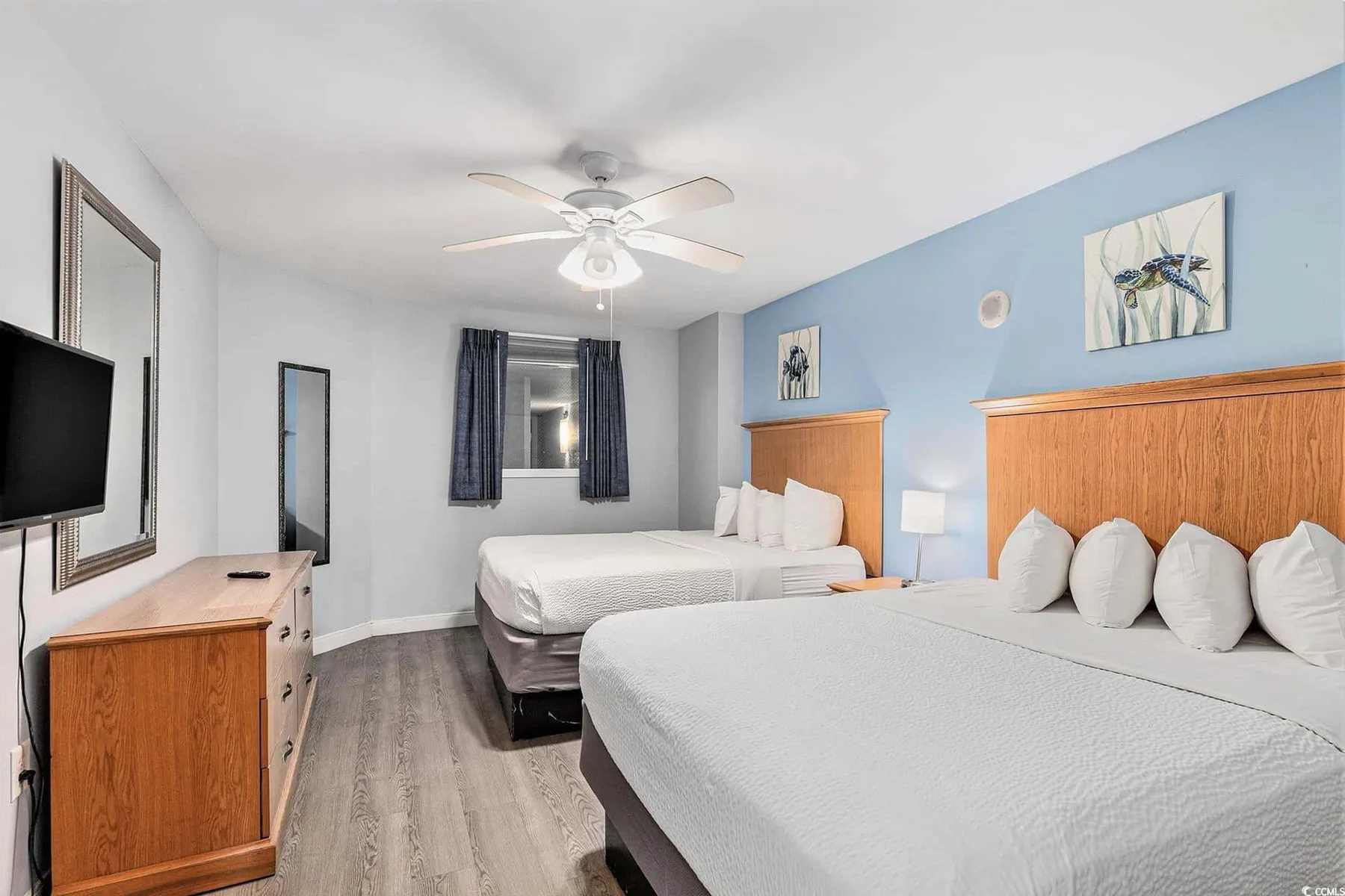 A bedroom with two beds, wooden headboards, and a window.