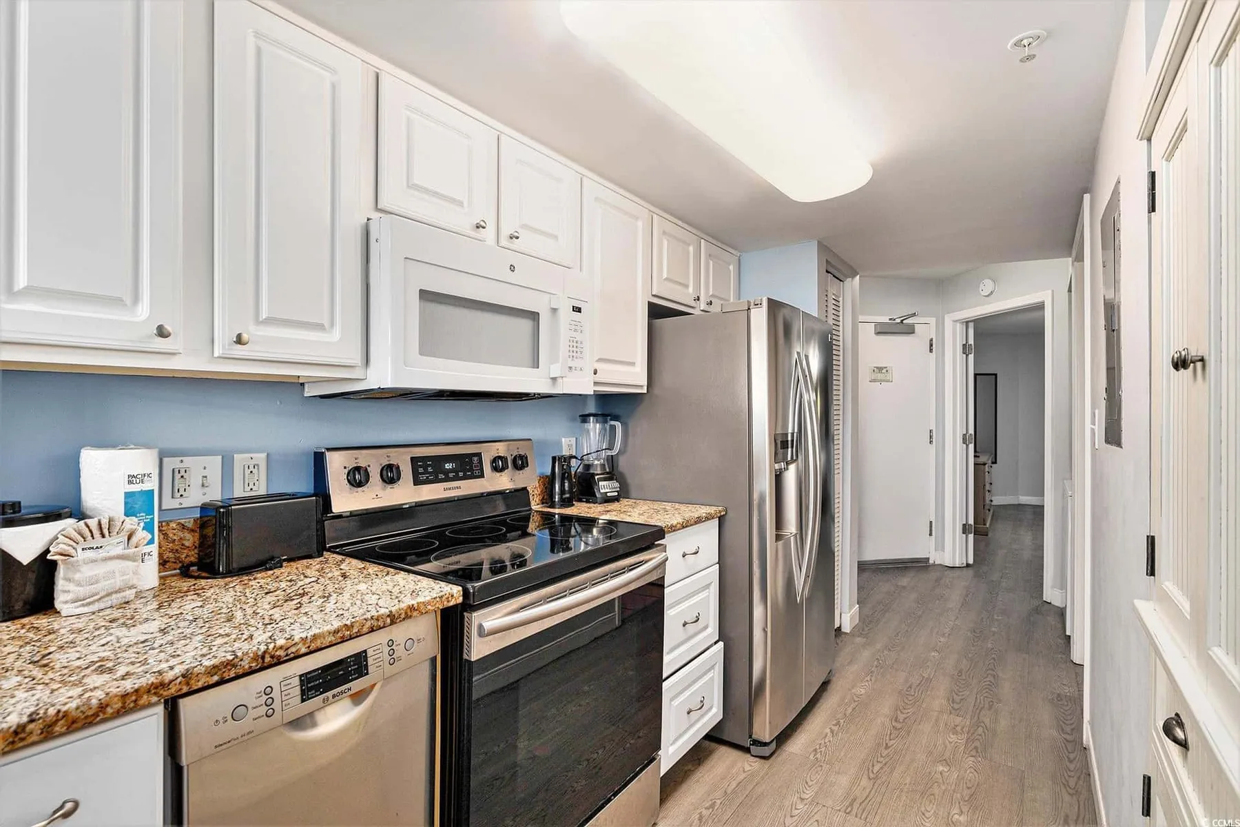 A bright kitchen with white cabinets, stainless steel appliances, and a granite countertop.