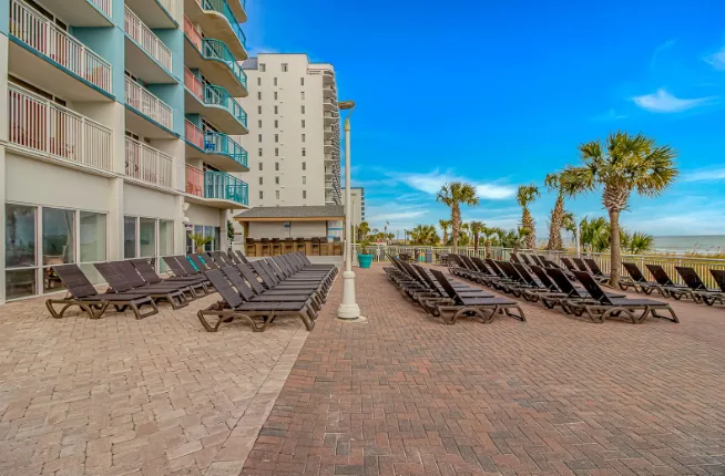 An outdoor poolside terrace has rows of lounge chairs beside a multi-story building.