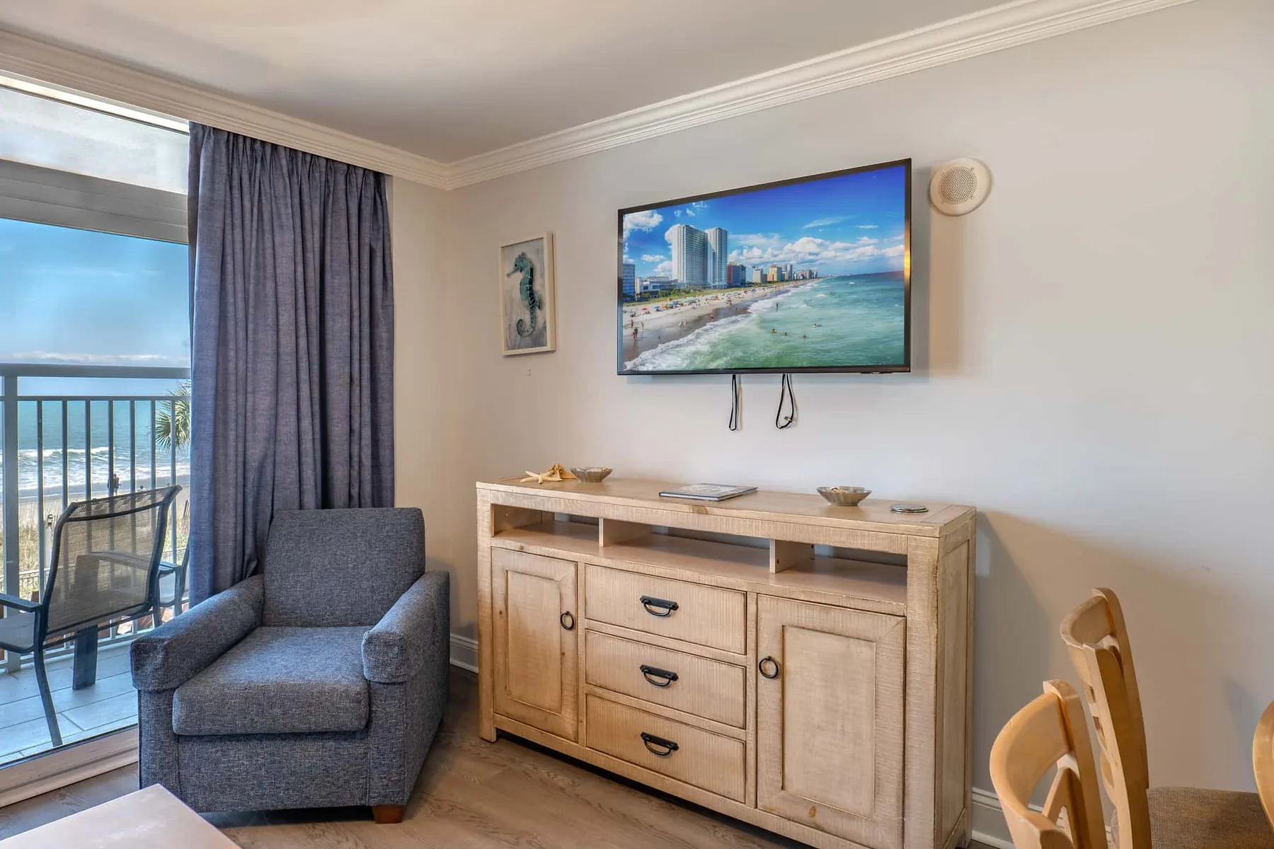A living area with a gray armchair beside a wooden dresser and wall-mounted television.