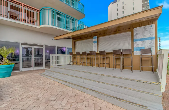 An outdoor bar counter with stools sits beside a paved patio.