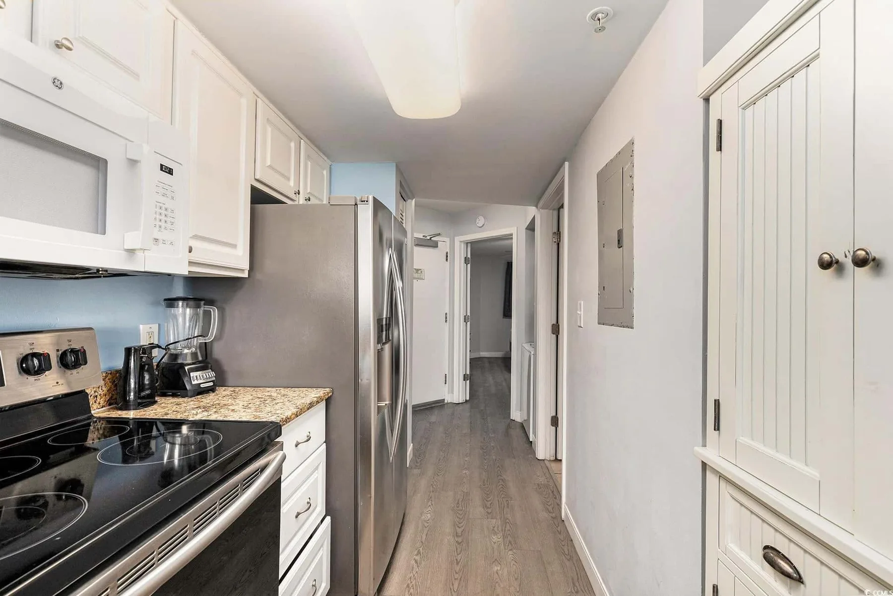 A kitchen opens onto a narrow hallway, with white cabinets and stainless steel appliances.