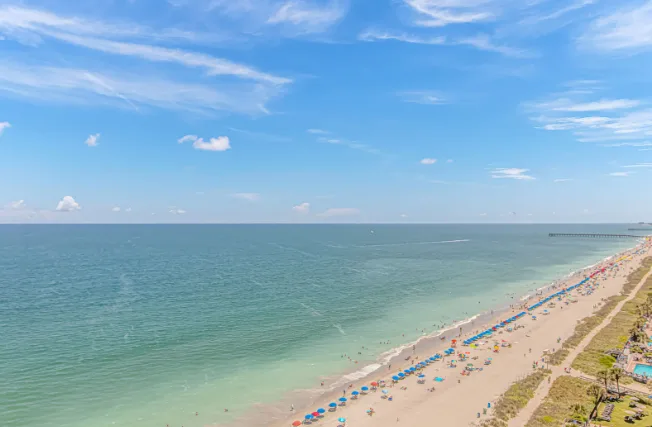 A sandy beach stretches along calm water beneath a bright blue sky.