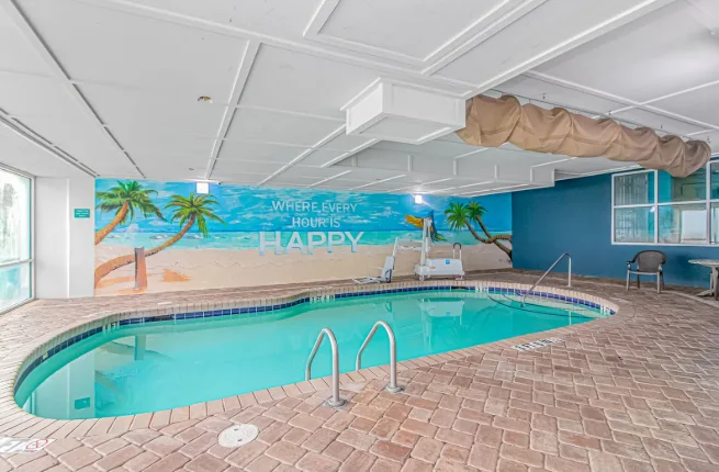An indoor swimming pool is surrounded by tiled flooring and a tropical beach mural.