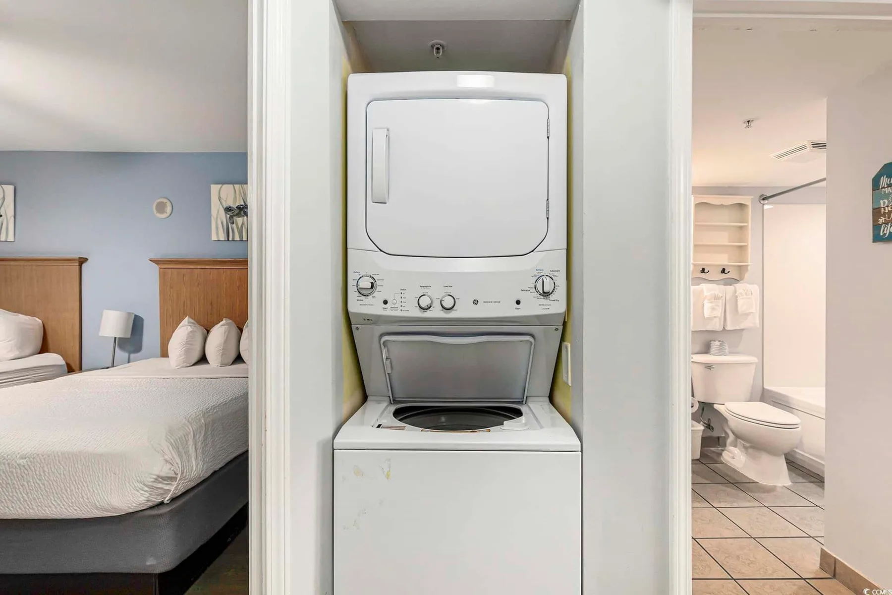A laundry area with a stacked washer and dryer between a bedroom and bathroom.
