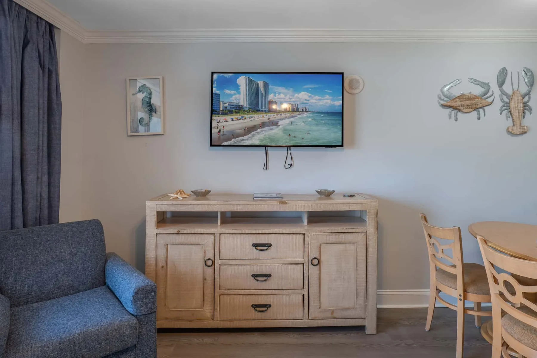 A living area with a television mounted above a wooden cabinet and seating nearby.