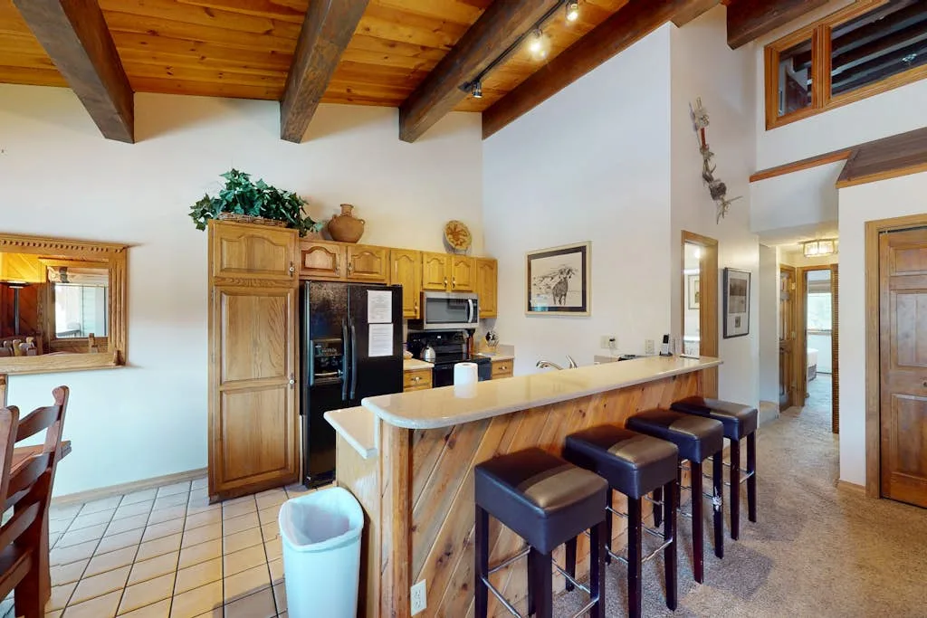 A kitchen with a wooden island, bar seating, and exposed ceiling beams.