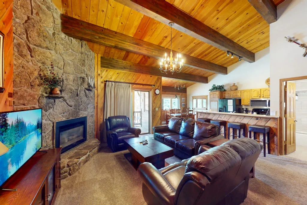 A rustic living room with leather seating, a stone fireplace, and a wood-paneled ceiling.