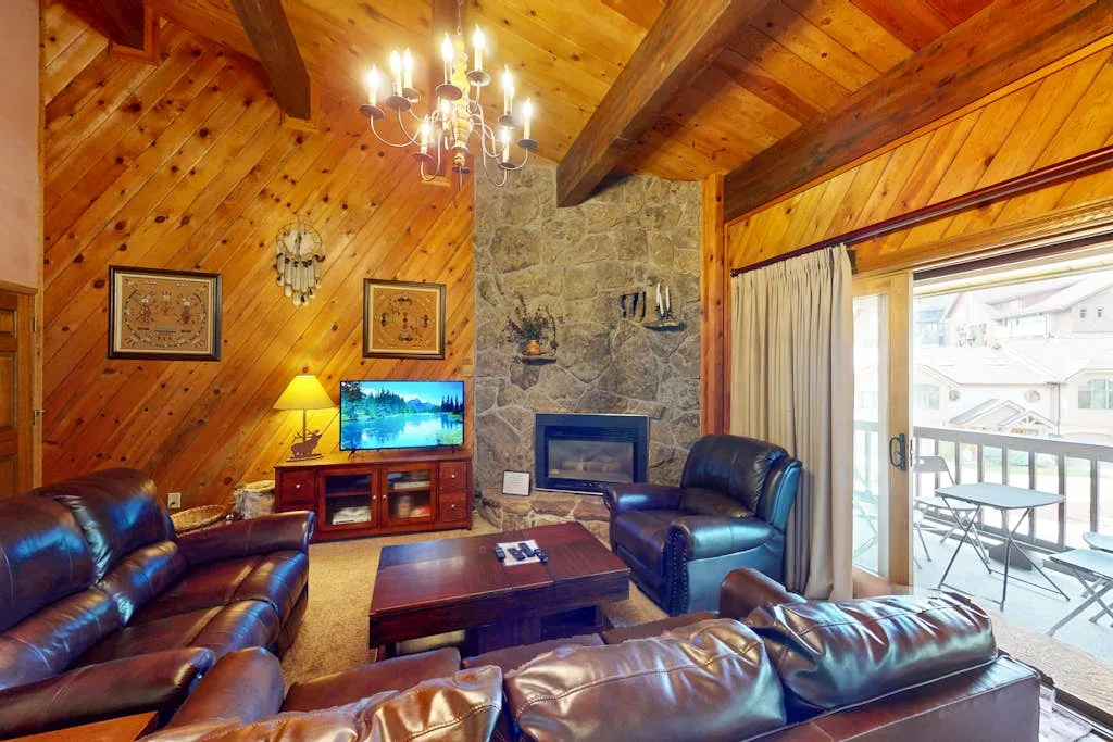 Sala de estar revestida de madera con asientos de cuero, televisor y chimenea de piedra.