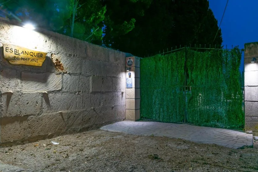 Un muro de piedra y una puerta verde bordean una zona exterior pavimentada de noche.