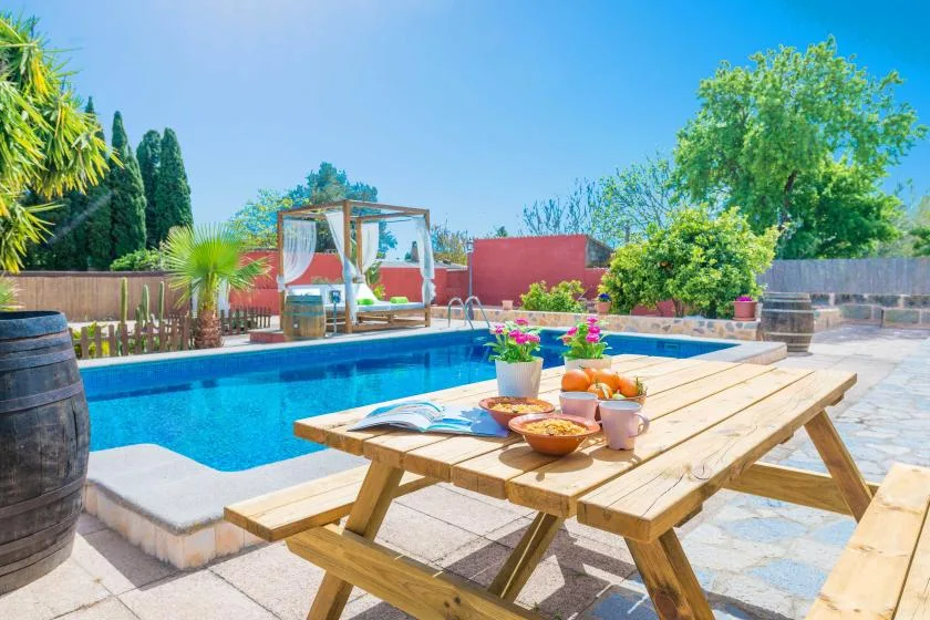 Una zona de piscina al aire libre tiene una mesa de picnic de madera con bebidas y comida.