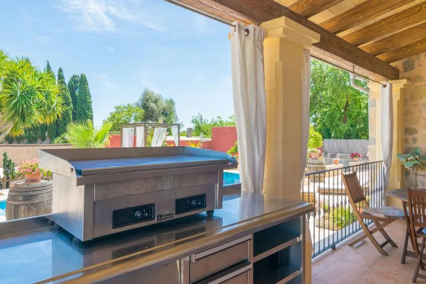 Un patio cubierto tiene una bañera de hidromasaje junto a asientos al aire libre y vegetación.