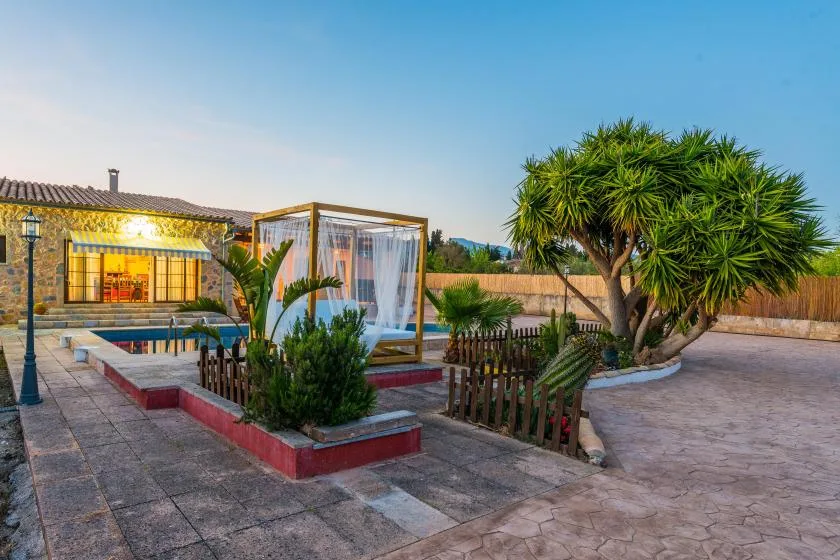 Una zona de piscina al aire libre con una cabaña con cortinas y árboles alrededor.