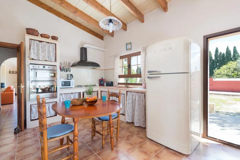 Una cocina luminosa con zona de comedor, asientos de madera y un refrigerador grande.