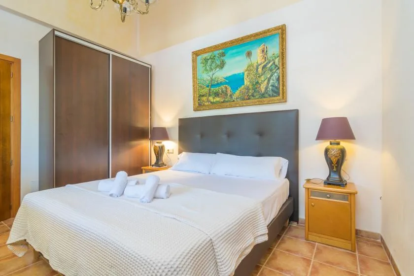 Dormitorio con una cama doble, mesitas de noche y un cuadro de paisaje enmarcado.