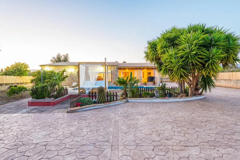 Una casa da a un patio pavimentado con parterres y árboles.