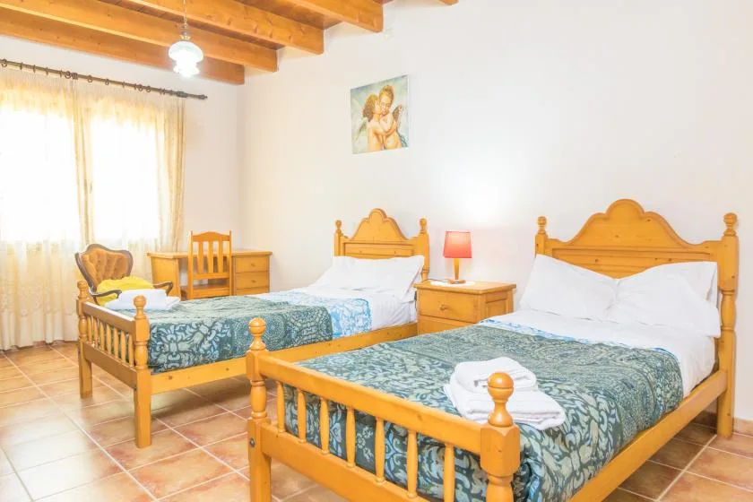 Un dormitorio con dos camas de madera, ropa de cama estampada y una ventana con cortinas traslúcidas.