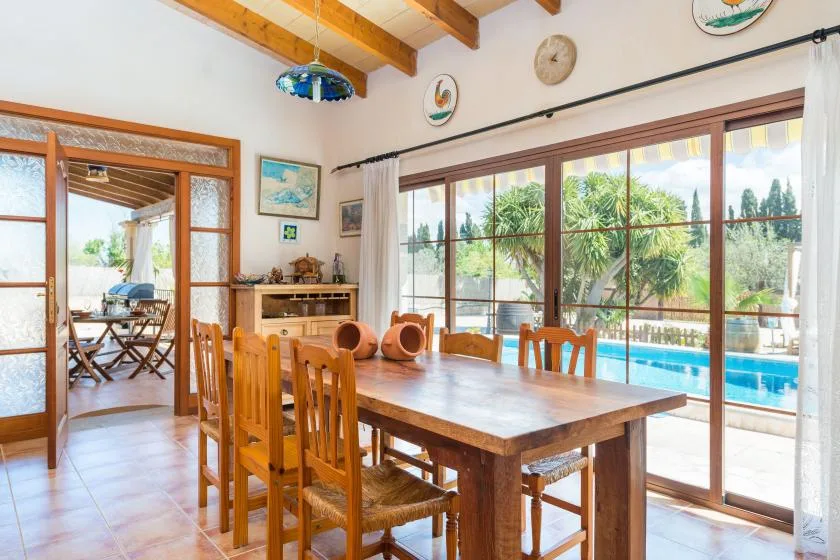 Un comedor con una mesa de madera junto a grandes ventanales con vistas a una piscina.